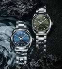 Two Omega Seamaster watches with blue and green dials on silver bracelets, displayed on dark textured surface